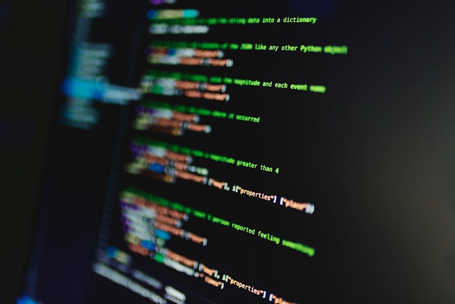 Close-up image of a computer screen displaying multicolored lines of programming code with syntax highlighting, including keywords in red, green, blue, and yellow on a dark background. The code featur